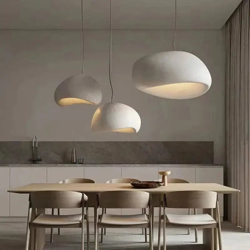 Designer Wabi Sabi pendant lights in white over dining area with wooden furniture. LED ceiling lamps add minimalist elegance to home decor.